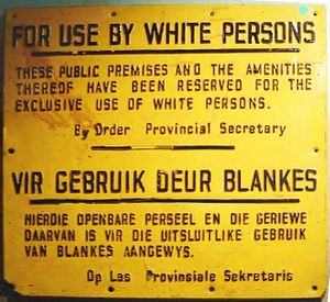 لافتة مكتوب عليها "للاستخدام من مقبل البيض. أنشئت هذه الأماكن العامة ووسائل الراحة ليستخدمها البيض حصريا." وبجانبها ترجمة للأفريكانية.