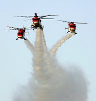 three helicopters flying in formation, making smoke trails in the sky