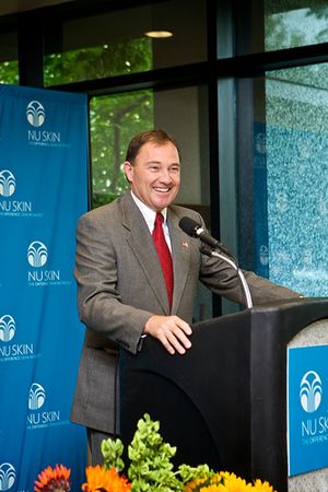 A man standing behind a podeum in a grey suit and red tie