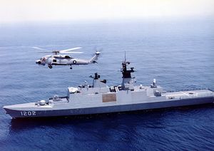 A light frigate on the sea above which a military helicopter is flying