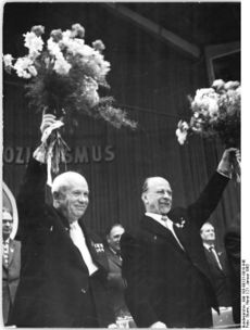 Two smiling men raise bouquets of flowers over their heads.