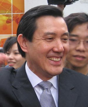 An East Asian man in suit smiling to the crowd