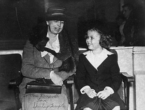Photograph of Eleanor Roosevelt seated with Temple immediately to her left. The two are looking at each other apparently engaged in conversation.