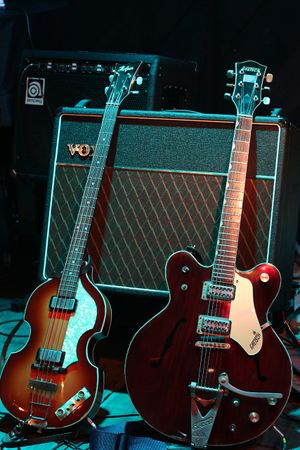 Two electric guitars, a light brown violin-shaped bass and a darker brown guitar, rest against a Vox amplifier.