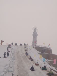 أشخاص يتريضون في الثلج بجوار تمثال للإلهة گوان‌ين في ووج‌ياچو.