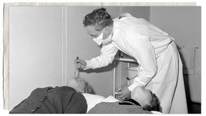 Dr. David Tyrrell places a common cold virus into the nostril of a patient during a research trial in 1966.jpg