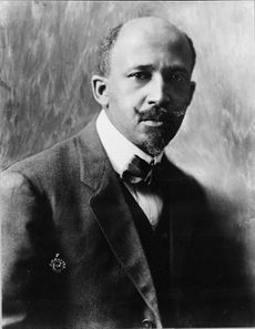 A dignified African-American man, with a mustache, dressed stylishly, sitting down.
