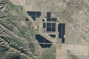 A satellite image of what look like semi-regularly spaced swathes of black tiles set in a plain, surrounded by farmland and grass lands