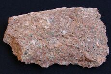 A rough chunk of granite showing grains of red, pink, white, gray and black.