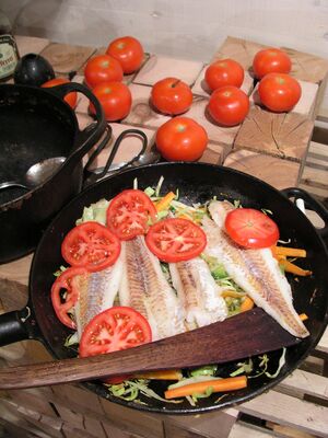 شرائح السمك فوق خضار مقطعة مطبوخة في مقلاة، ومغطاة جزئيًا بشرائح الطماطم.