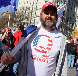 Man wearing a t-shirt with a design consisting of a block letter "Q" overlaid with an American flag pattern