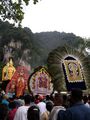 Icons carried in procession during Thaipusam at Batu Caves. Also seen in the background is the 42.7 m high golden statue of Murugan.