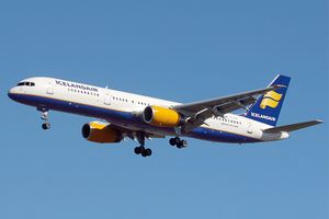 A mostly white Boeing 757 with blue and yellow trim preparing for landing against a blue sky. Landing gear and flaps are extended in final approach configuration.