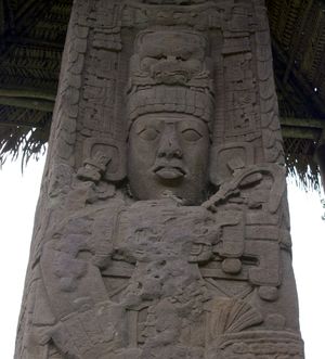 Close up of upper portion ofan intricately carved stela, showing the face of a king with elaborate headdress and jewellery