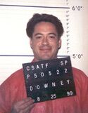A mugshot of actor Robert Downey Jr smiling for his headshot in 1999