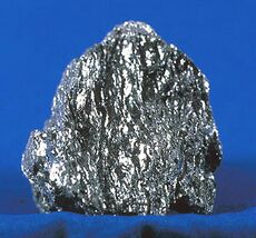 A sparkling, metallic gray chunk of hematite on a blue background.