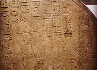 Rock stela covered in hieroglyphs and showing two standing figures, on the left the god Osiris, on the right a woman offering him incense.