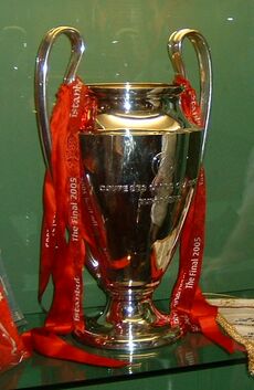 A silver trophy with red ribbons on it, set against a green background