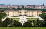 Rocoo three and four story palace stretches across most of the midground. In the foreground are manacured lawns and walkways, while the background is the old city of Vienna with a cathedral on the horizon.