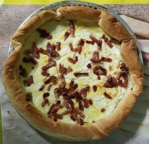 round tart with yellow filling and bacon bits on the top