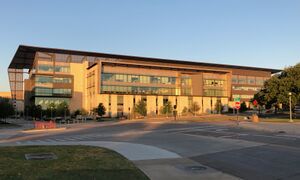 A five-story, tan building behind a street and sidewalk.