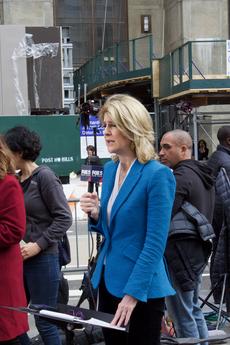 A white woman in a light blue blazer holds a FOX 5 New York-emblazoned microphone.