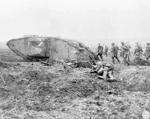 A group of soldiers with guns march on uneven ground past a wrecked tank and the body of another soldier