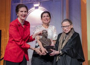 Three women gripping a bust and smiling