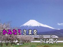 Over a background image of Mount Fuji and a Shinkansen train two lines of Japanese text. The first half of the first line is colored red-violet, the rest white. The text reads "かみなりさまを　下 に聞く".