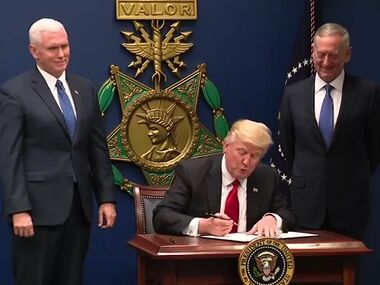 Donald Trump signing the order in front of a large replica of a USAF Medal of Honor, with Mike Pence and James Mattis