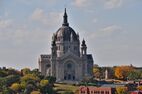 A towering gray stone cathedral with a round copper roof stands above autumn trees.