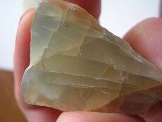 A chunk of grayish yellow moonstone which shows fracture lines and a blue glow in some portions.