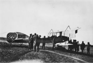A group of men gather around a biplane. The Union Jack has been painted on to the tail of the aircraft.