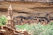 Remnant dwellings of the ancient Tellem people in the background, above the abandoned Dogon village; a mud mosque of the modern-day Dogon village is visible in the foreground