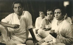 Photograph of Satyajit Ray seated with Ravi Shankar with several others in the background
