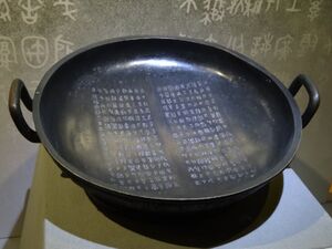 a broad bronze pan with two handles and a lengthy inscription on the flat area inside