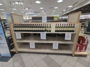 A shelf in a liquor store, it is empty except for the top shelf