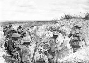 Heavy laden soldiers move through a communication trench during the daytime.