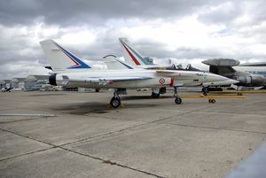 Side view of white jet aircraft parked with other aircraft in the background