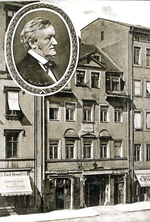 A postcard of a five-story building with shops on the ground floor and garret windows in the roof. A round inset has a picture of Wagner in middle age.