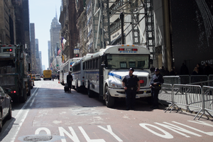 أربع حافلات مدرسية مطلية باللونين الأزرق والأبيض مصطفة على جانب شارع مزدحم في مانهاتن.