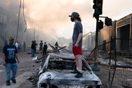 A man stands on a burned out car as fires burn behind him in the Lake St area of Minneapolis.