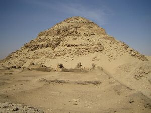 The prominent but crumbling remains of a pyramid, with its original, well-preserved stepped structure exposed underneath the rubble