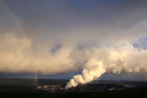 A rainbow is to the left, as a plume of volcanic ash drifts to the right.