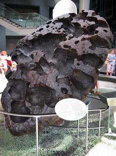 A large black egg-shaped boulder of porous structure standing on its top, tilted