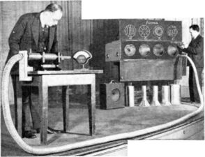 ساوثوورث (على اليسار) يعرض الدليل الموجي في اجتماع معهد مهندسي الراديو عام 1938، ويظهر موجات ميكروويڤ بتردد 1.5 گيگاهرتز تمر عبر خرطوم معدني مرن بطول 7.5 متر مسجل على كاشف الصمام الثنائي.