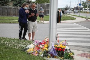 رجل وامرأة من سكان مدينة لندن الكندية يضعون أكاليل الزهور في موقع حادث دهس الأسرة الپاكستانية، 8 يونيو 2021.