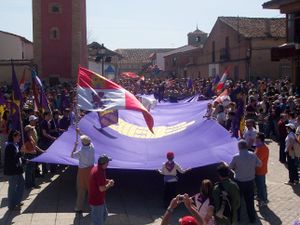 People at a celebration holding a huge purple flag. Others wave different flags, such as the Cross of Burgundy or the modern flag of Castile and León.