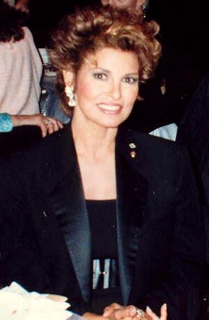 Welch in a dark scoop top, wide belt, and tuxedo-styled jacket, hair styled up