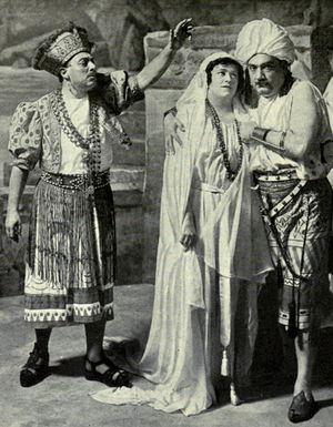 Three figures in exotic costumes; to the right a man and a woman embrace, while on the left another man addresses them, left arm raised perhaps in a gesture of blessing